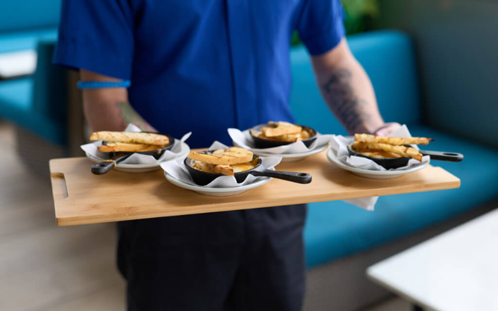 Server carrying a tray of 4 iron skillets filled with delicious food